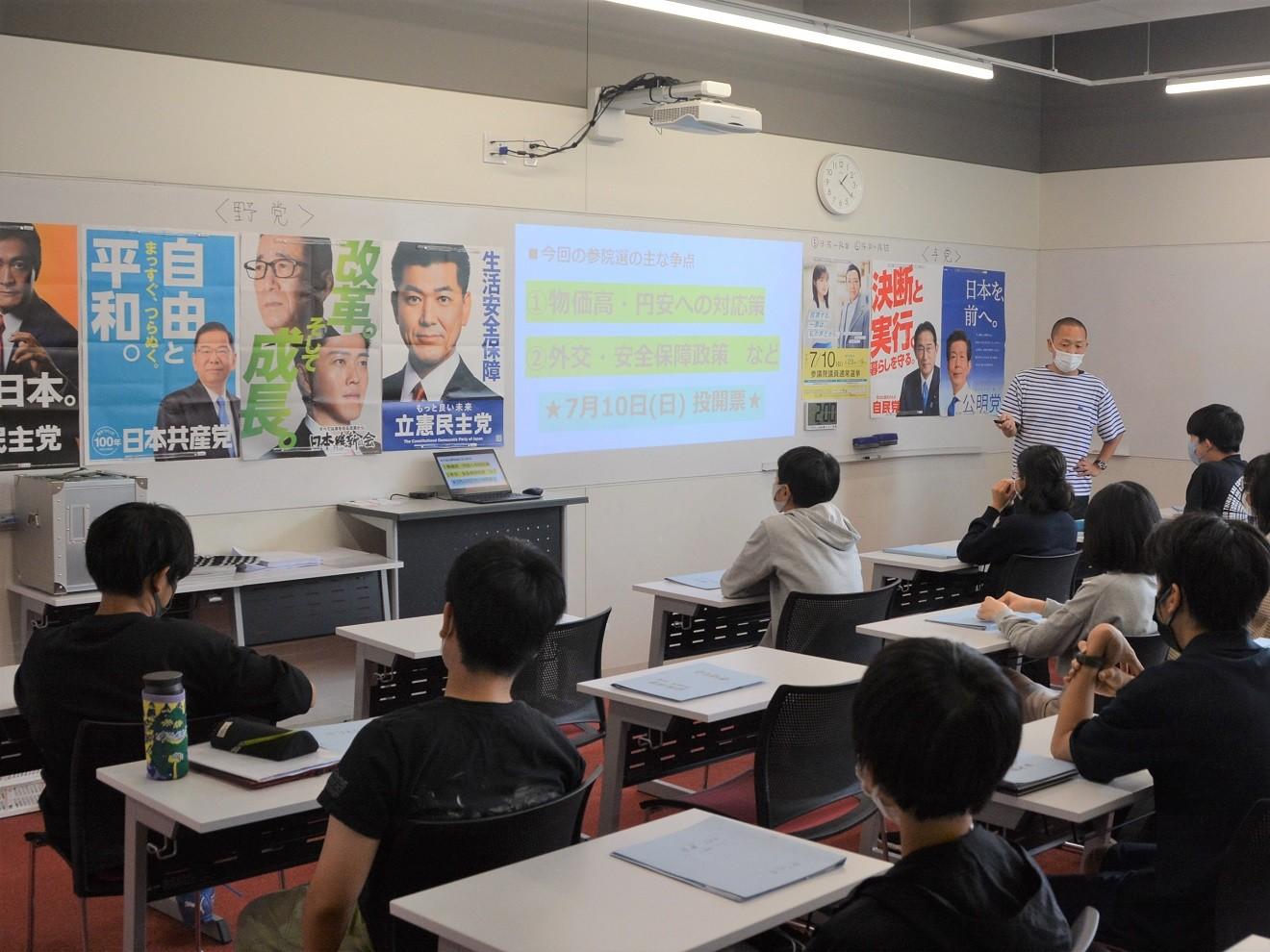 政党ポスターの前で語る大畑方人先生